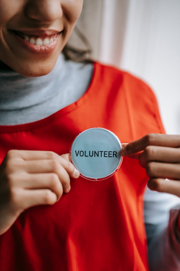 our-mission Close-up of a smiling volunteer holding a badge in a bright setting.